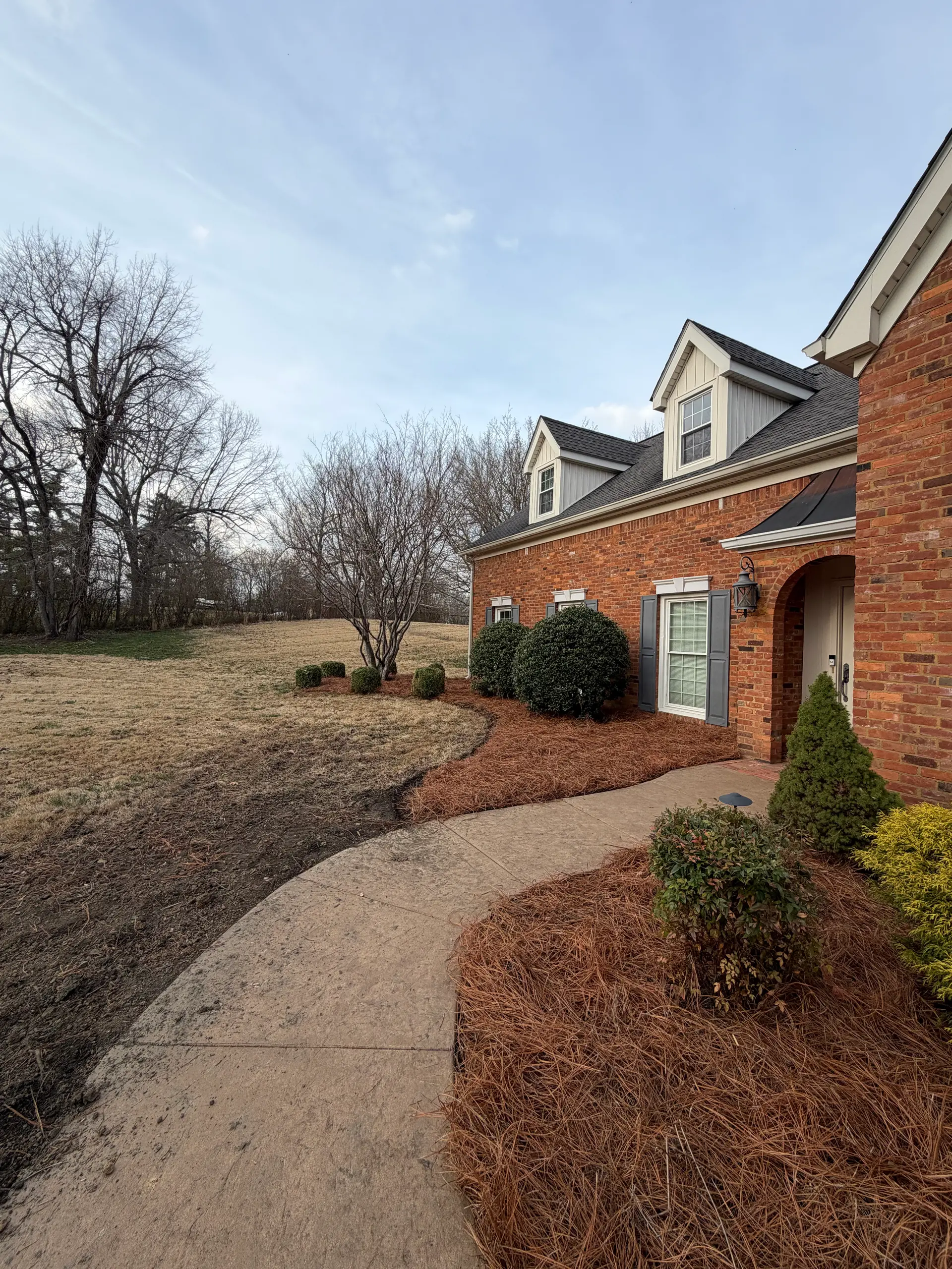Curved walkway and pine straw beds at a brick home landscaped by Luxury Lawns